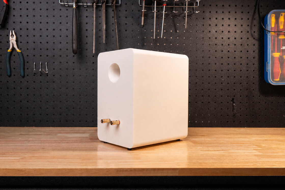 White speaker on a wooden workbench with tools hanging on a pegboard in the background.