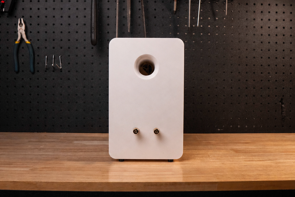 White speaker on a wooden workbench with tools hanging on a pegboard in the background.