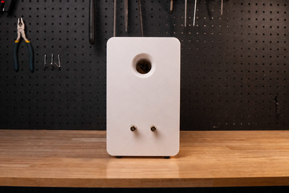 White speaker on a wooden workbench with tools hanging on a pegboard in the background.