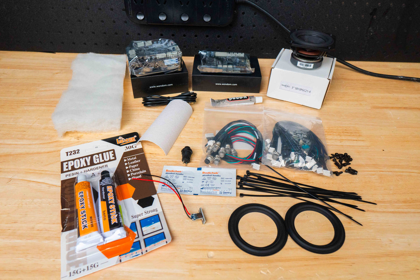Electronic components and tools on a wooden surface including a bluetooth amplifier, speaker driver batteryboard and cable kits