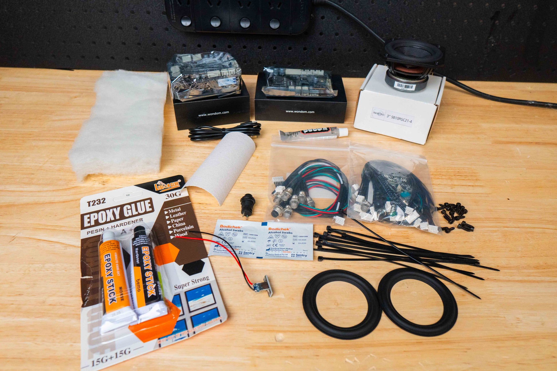 Electronic components and tools on a wooden surface including a bluetooth amplifier, speaker driver batteryboard and cable kits