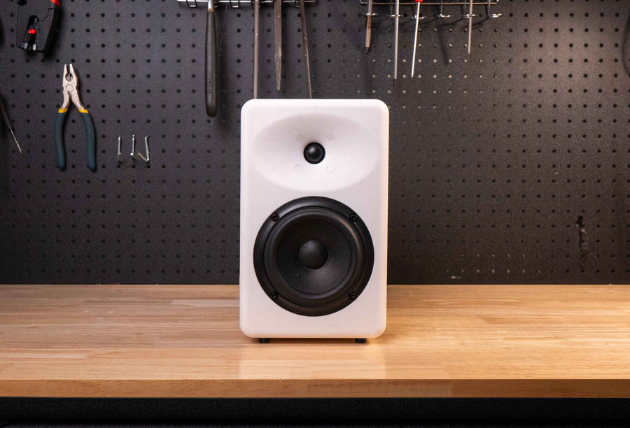 White speaker on a wooden desk with tools hanging on a pegboard wall.